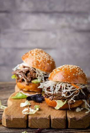 Pulled beef burger with cabbage salad and bbq sauce on cutting boardの写真素材