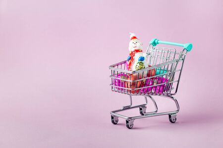 shopping cart full of christmas presents on bright pink backgroundの写真素材