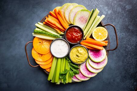 Buddha bowl of mixed raw snacks. vegetables with sauces carrots, cucumber, persimmon, celery and radishes, top view, flat layの写真素材