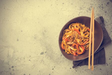 Asian food, stir fry udon noodles with meat and vegetables in a bowl on gray stone background, top viewの写真素材