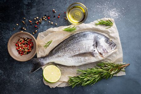 Fresh ready to cook raw bream fish dorado with ingredients and seasonings like rosemary, salt, pepper, lime and olive oil, top viewの写真素材