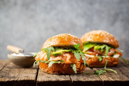 Burger sandwich with salmon, cream cheese, avocado and arugula on a light background, concept diet food, take away, healthy fast foodの写真素材