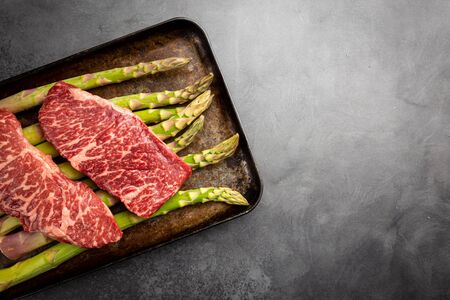 Raw Steak with green asparagus on tray on black background, top viewの写真素材