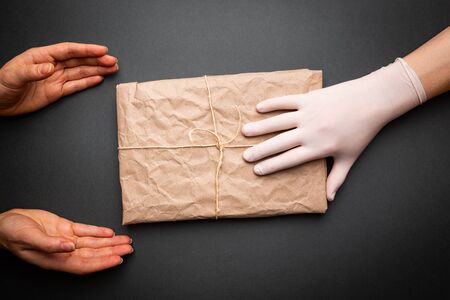contactless delivery concept, gloved hands transmit the package with corona virus protect. Safe courier deliveryの写真素材