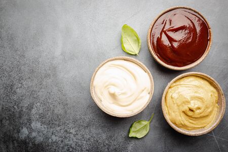 Classic set of sauces, American yellow mustard, ketchup, barbecue sauce, mayonnaise on black stone...