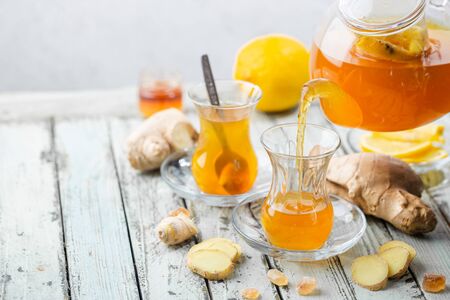 Ginger tea in a glass cup with lemon and mint on light background