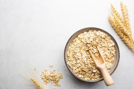 Rolled oats or oat flakes in bowl and wooden spoon on white table, top view with copy space