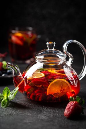 Fruit red tea with berries in glass teapot on black backgroundの写真素材