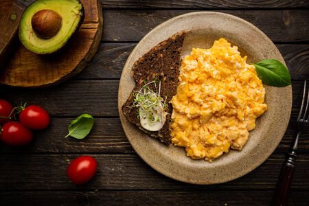 Fresh cooked scrambled eggs in a plate on dark rustic wooden background, top viewの写真素材