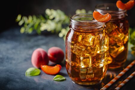 Glass of peach or apricot iced tea with fruit slices against dark blue backgroundの写真素材