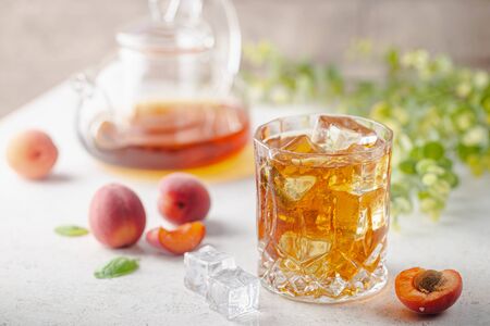Glass of peach or apricot iced tea with fruit slices against white backgroundの写真素材