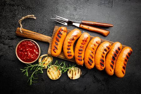 Fried delicious sausages with tomato sauce and herbs on cutting board, top view, black background.の写真素材