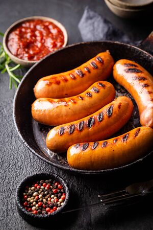 Fried delicious sausages with tomato sauce and herbs in a pan, black background.の写真素材