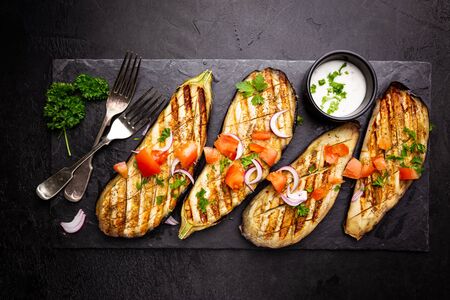 Grilled eggplant slices, garnished with fresh herbs, on black background, top viewの写真素材