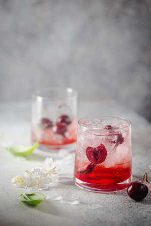 Cold cherry lemonade drink with fresh cherry and ice on gray background