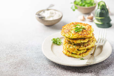 Green zucchini fritters, vegetarian zucchini pancakes with fresh herbs and garlic, served with cream sauce on white background, selective focusの写真素材