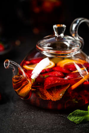 Fruit red tea with berries in glass teapot on black backgroundの写真素材
