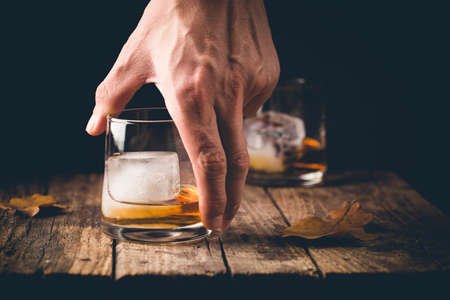 Glass of scotch whiskey and ice on wooden background with handの写真素材