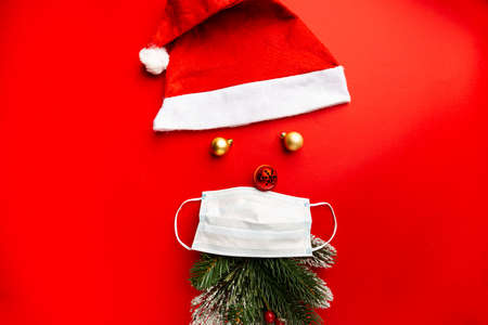 Coronavirus Christmas santa hat with protective mask on red background with copy space. Covid-19...