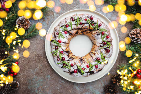 Traditional homemade christmas cake holiday dessert with cranberry and chocolate with new year tree decoration on vintage wooden table background. Rustic style.の写真素材