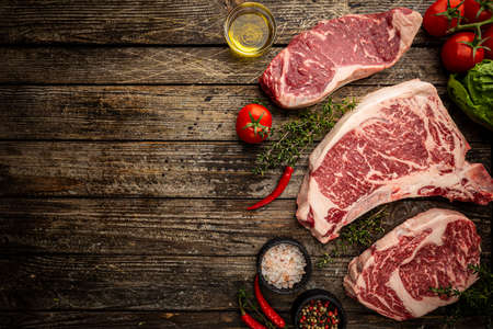 Variety of Fresh Raw Black Angus Prime Meat Steaks T-bone, New York, Ribeye and seasoning on wooden background, top viewの写真素材