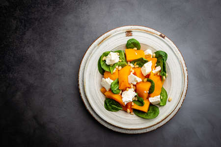 Salad with roasted pumpkin, cheese, spinach, Pine nuts and seasonings on dark background, top viewの写真素材