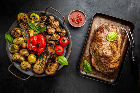 Baked pork meat with grilled vegetables in a baking pan on dark background, top viewの写真素材