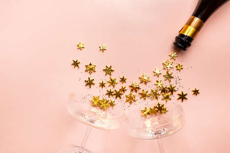 Champagne bottle with golden glittering splashes and champagne glasses on pink background. Flat lay,...