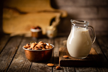 Vegan alternative non dairy milk from almond nuts in a jug with various nuts on wooden tableの写真素材