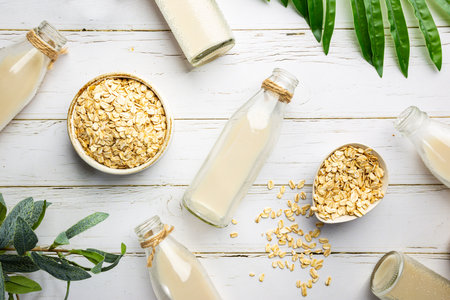 Vegan non dairy oatmeal milk in bottles on white wooden background. Lactose free milk substitute. Top view.の写真素材