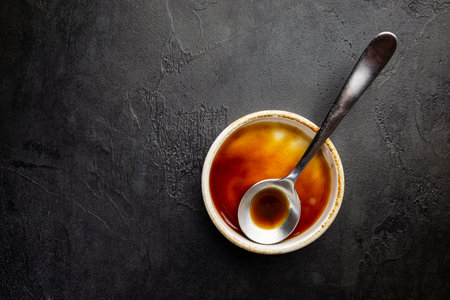 Worcestershire sauce in a bowl with spoon over black background, top viewの写真素材