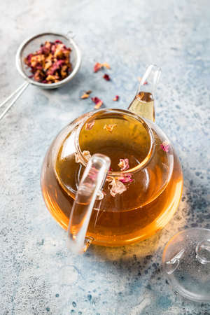 herbal flower tea from the petals of rose in a glass teapot on light blue background, top view