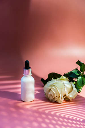 Serum or essential oil bottle on pink background with rose flower. Beauty product concept.の写真素材