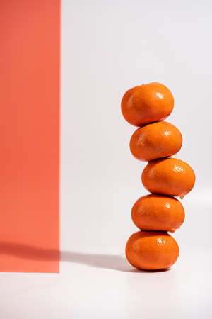 Stacked tangerines isolated on white and orange background. Healthy eating. Minimalism and balance concept with bright shadowsの写真素材