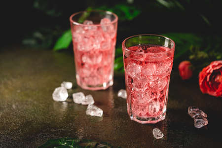 Red drink cocktail or lemonade with ice in a glass on dark background.