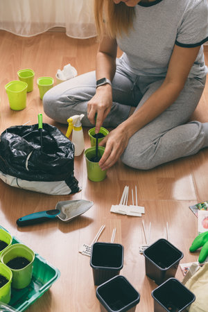 Young woman plant seedlings at home on the floor. Hold the garden toolsの写真素材