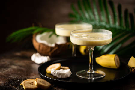 banana cocktail with coconut milk in a glass on dark background with palm leavesの写真素材