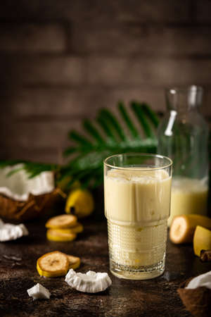 banana cocktail with coconut milk in a glass on dark background with palm leaves