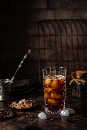 Ice coffee in a tall glass with sugar and coffee beans on dark background