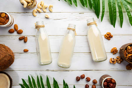 Vegan non dairy nut milk in bottles and various nuts on white wooden background. Lactose free milk...