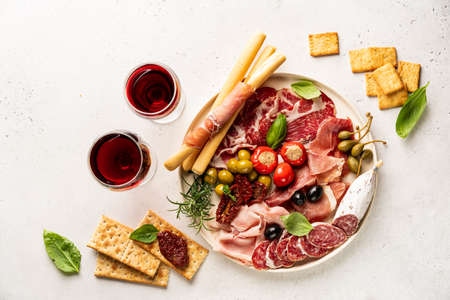 Appetizers with differents antipasti, charcuterie, snacks and red wine on white background. Sausage, ham, tapas, olives and crackers for buffet party. Top view, flat layの写真素材
