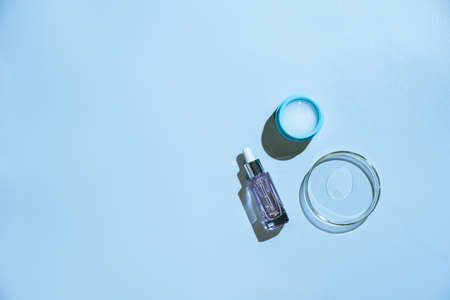 Different glass bottles with serum or oil and cosmetic skin care cream on blue background. Trending shadow. Cosmetic mockup. Top view with copy space. Flat lay.の写真素材
