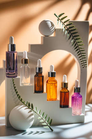 Glass cosmetic bottle with oil or serum for skin care on special podium on apricot color background. Natural skin care concept. Harsh shadowsの写真素材