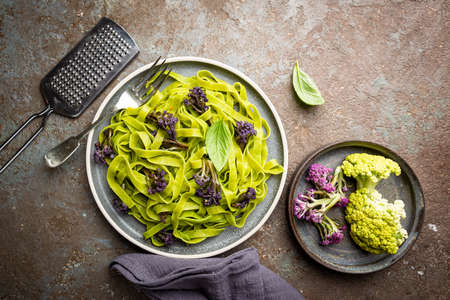 Green Tagliatelle pasta with purple cauliflower on gray background, top view
