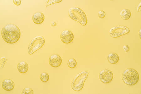 Yellow background with cosmetic lotion or transparent gel drops and smears with glitter