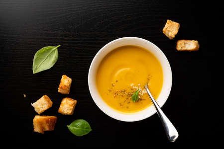 Vegetable vegetarian cream soup in a white bowl with croutons on a black wooden background, top viewの写真素材