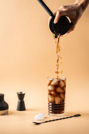 Soft drink Cola or cuba libre cocktail in a glass with ice cubes isolated on light orange backgroundの写真素材