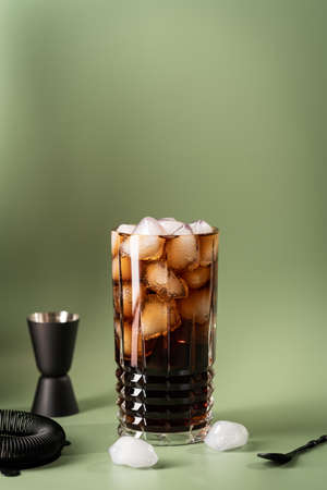 Soft drink Cola or cuba libre cocktail in a glass with ice cubes isolated on green backgroundの写真素材