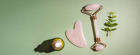 Jade face rollers and Gua sha stones for beauty facial massage therapy, Items for home treatment with Skin Care Anti-Aging Tools and Face Serum on green background, top viewの写真素材