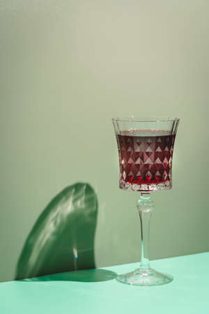 Wine Glass of red wine with bright shadows over green backgroundの写真素材